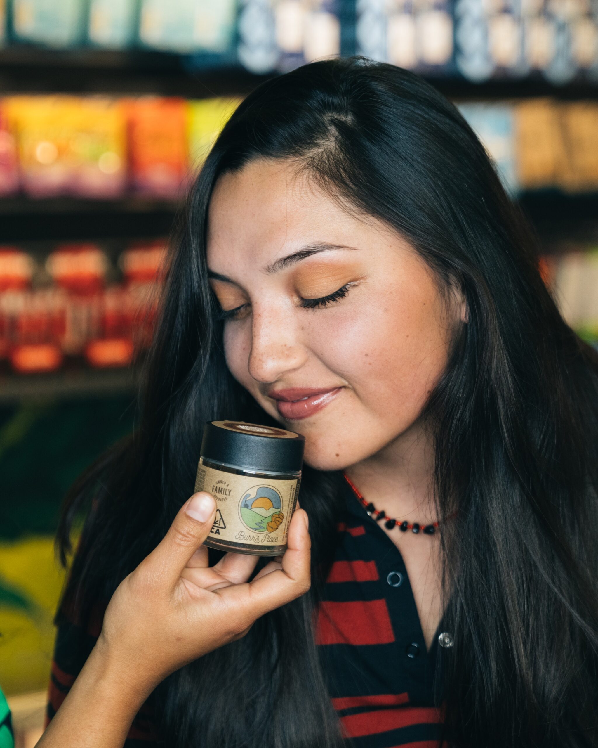 woman smelling jar of cannabis in front of wall of cannabis products