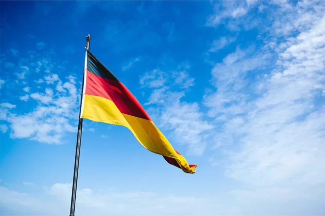 german flag blowing in the wind on a flagpole on a blue sky day with some light clouds