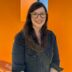 woman smiling in glasses in black jean jacket with long hair in front of orange wall