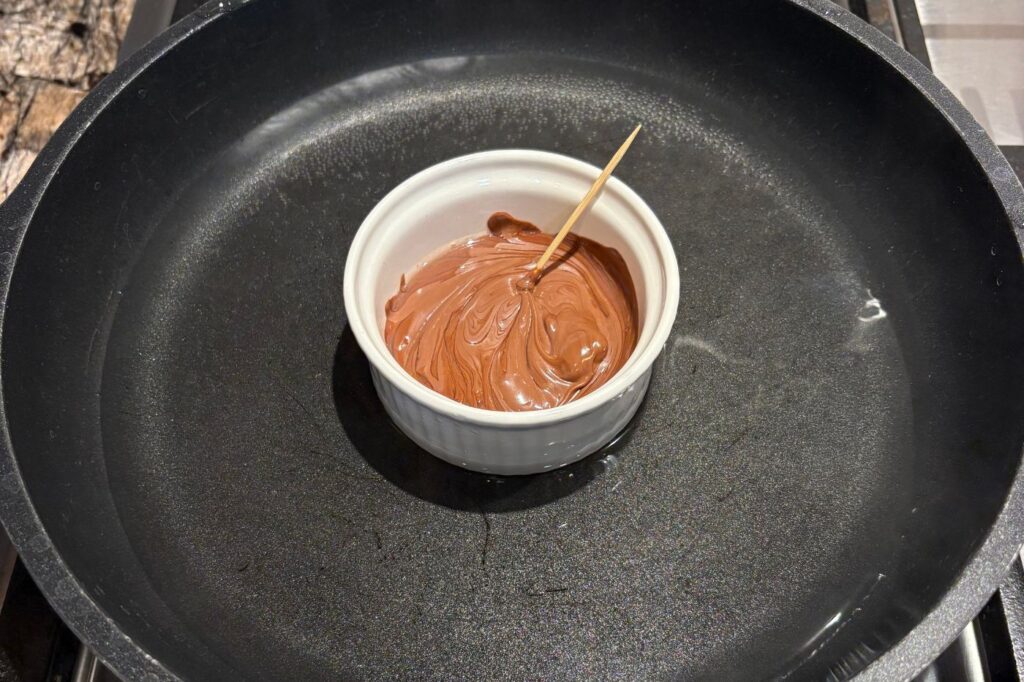 melting chocolate in a double boiler with a pan and ramekin on the stove with toothpick to stir
