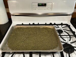 ground cannabis flower spread across a cookie sheet for decarbing in the oven