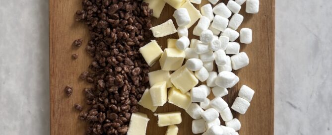 ingredients for edibles rice krispy treats with butter, salt, vanilla extract, marshmallows, and chocolate rice crispy cereal on a cutting board