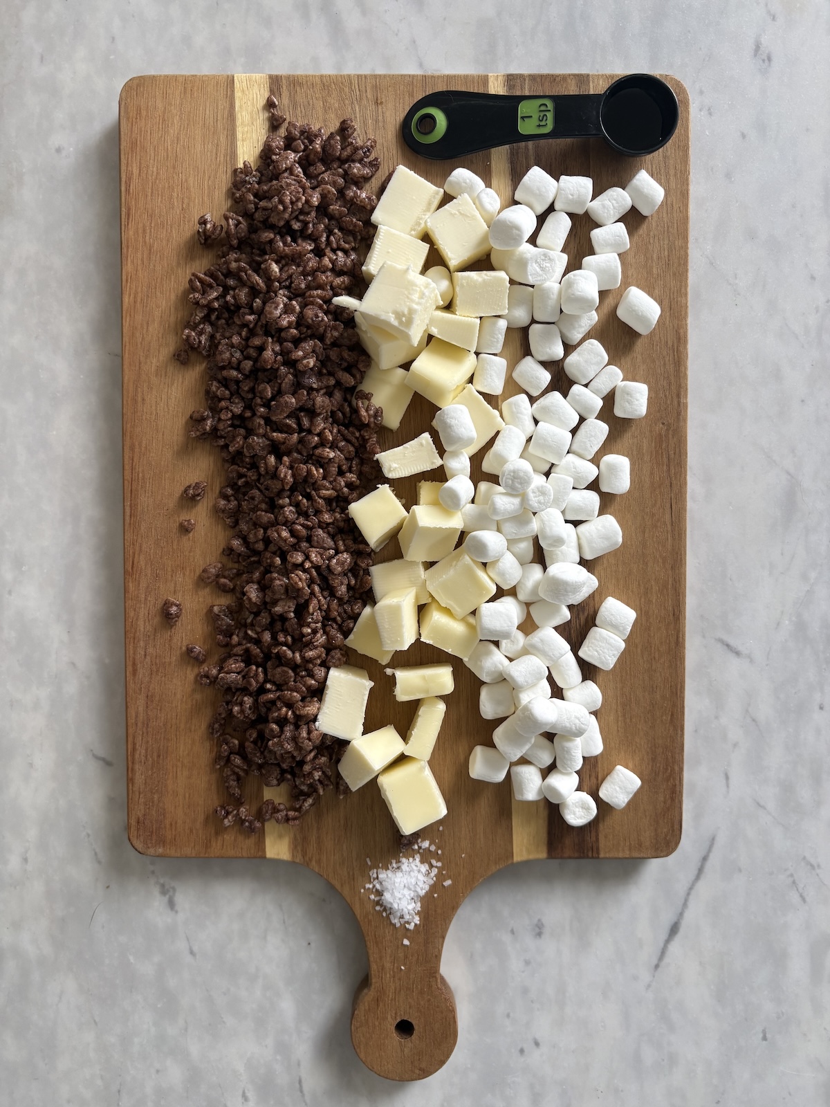 Ingredientes para golosinas comestibles de Rice Krispies con mantequilla, sal, extracto de vainilla, malvaviscos y chocolate; cereales Rice Krispies sobre una tabla de cortar